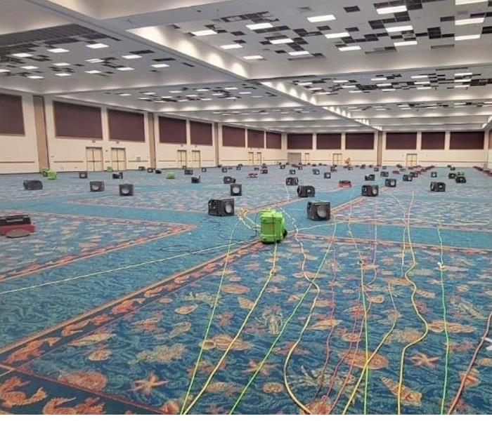 Large room with SERVPRO equipment set up on the blue and coral carpeting